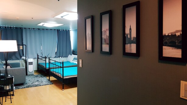A modern bedroom with a bed, bedside table, lamp, and a view of a cityscape through a window. - Justin House (Seoul)