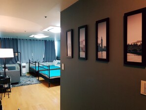 A modern bedroom with a bed, bedside table, lamp, and a view of a cityscape through a window. - Justin House (Seoul)