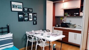 A compact room with a bed, a dining table with chairs, a kitchenette, and framed pictures on the wall. - Justin House (Seoul)