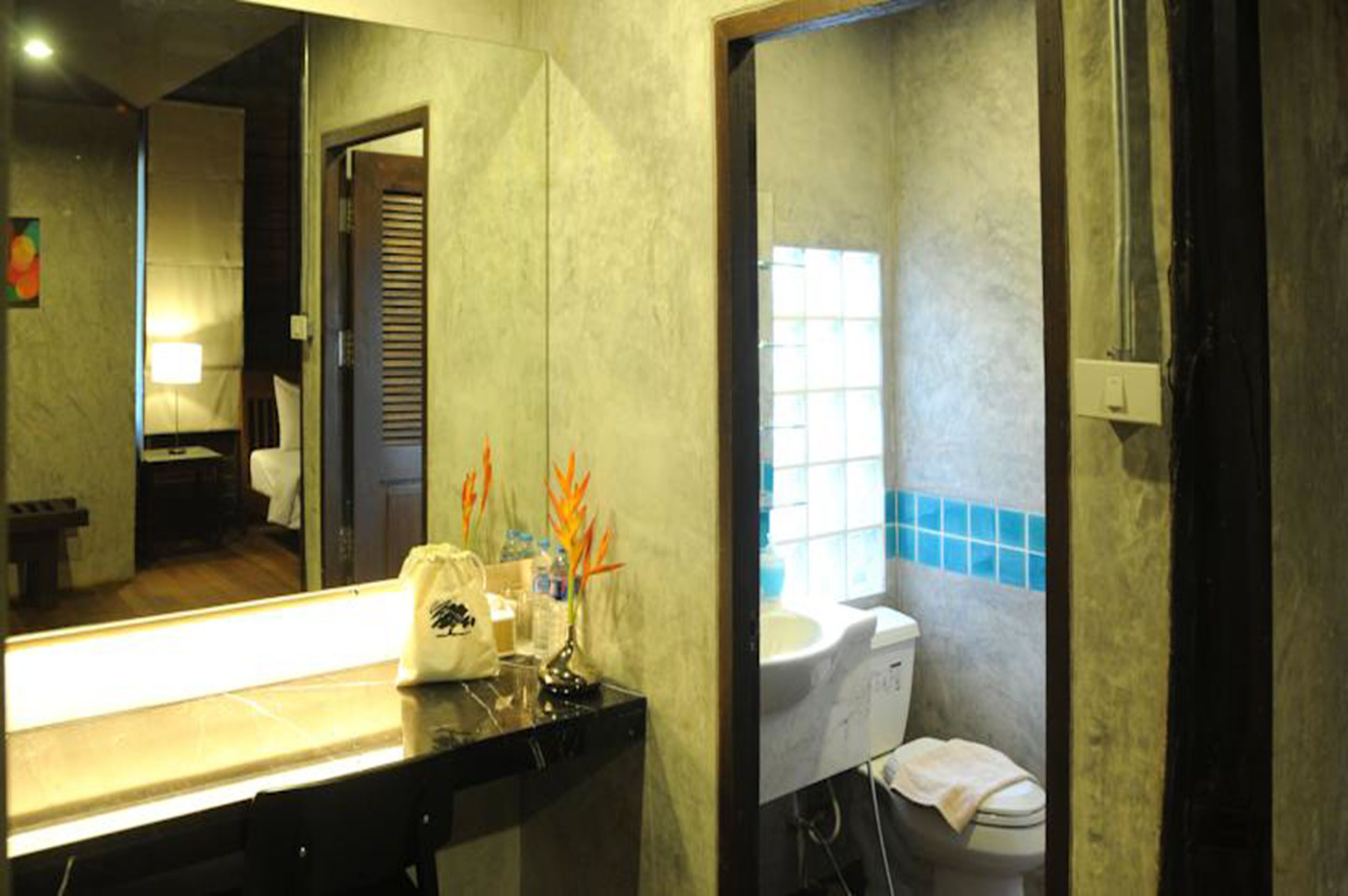 A bathroom with a large mirror, a sink, and a toilet. There is a towel hanging on the wall and a small plant on the counter.