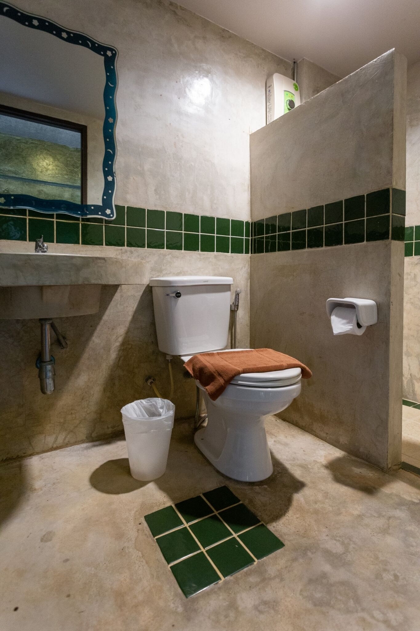 Baño con inodoro, lavamanos y paredes de azulejos verdes.