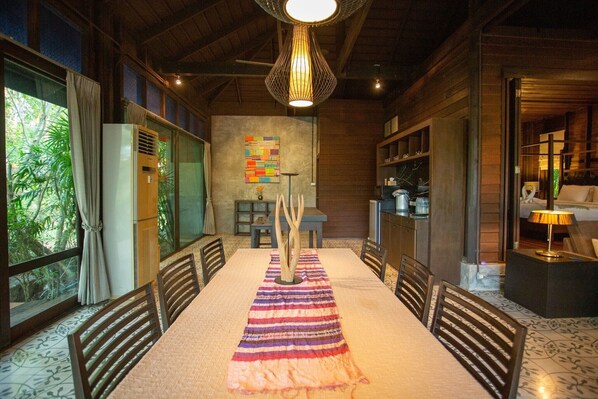 A dining area with a long table, chairs, a decorative centerpiece, and a hanging light fixture.