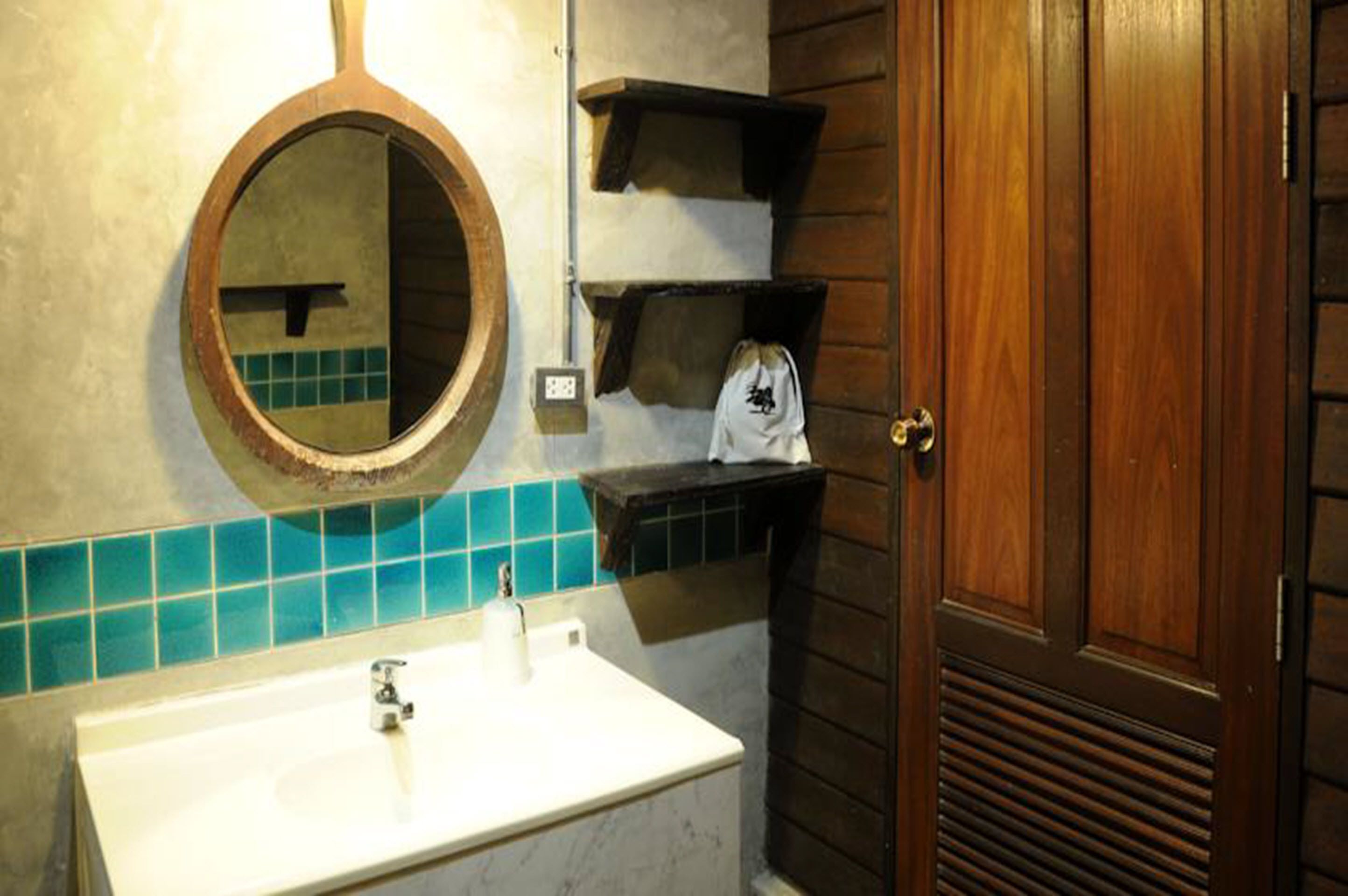 Une salle de bain avec un lavabo blanc, un miroir rond et des étagères en bois.