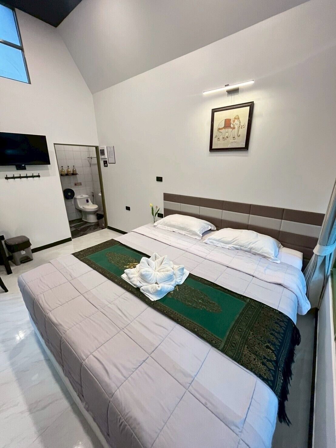 A modern hotel room with a large bed, a television, and a bathroom with a toilet and sink.