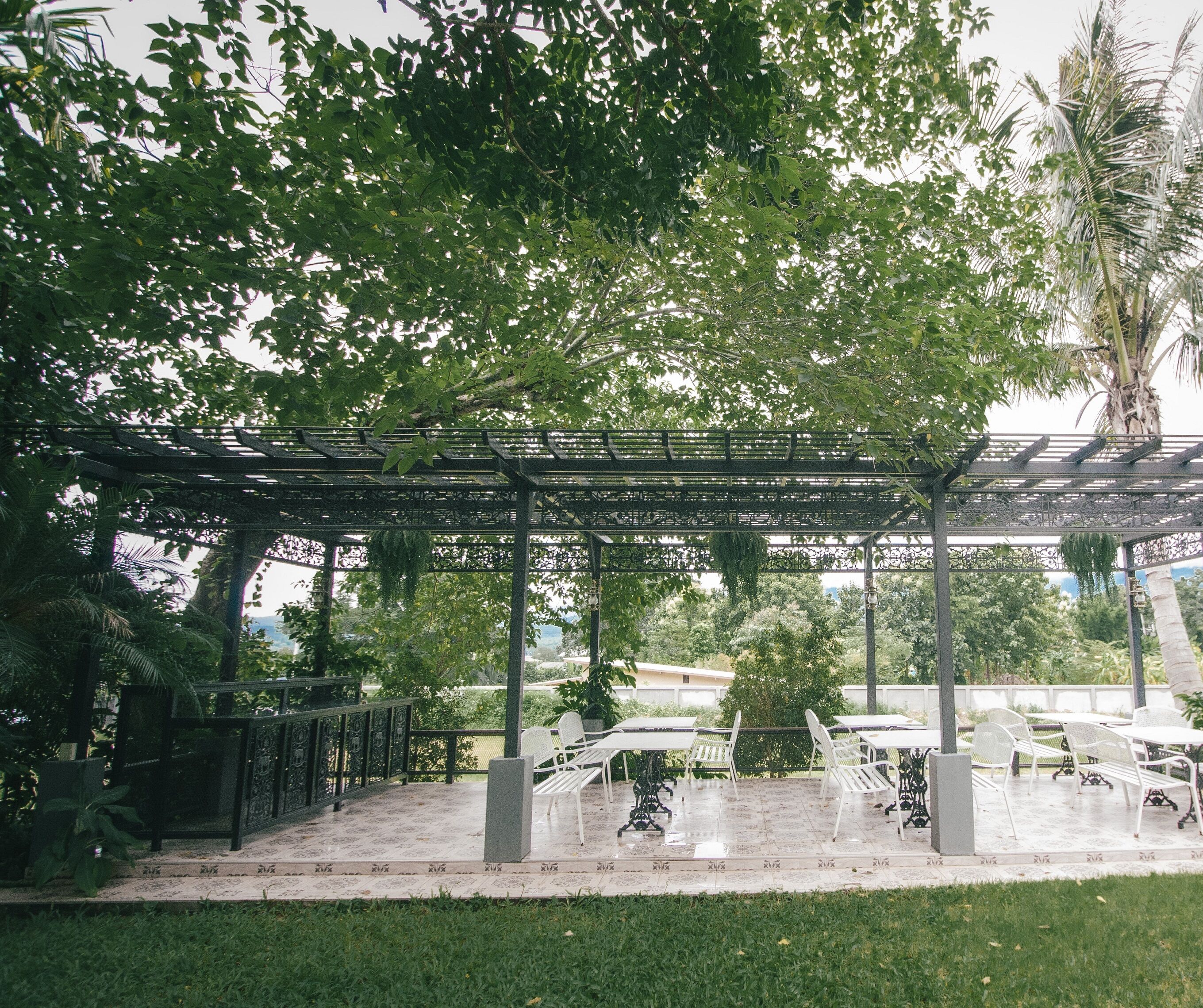 Et udendørs opholdsområde med pergola, hvide metalstole og et bord.