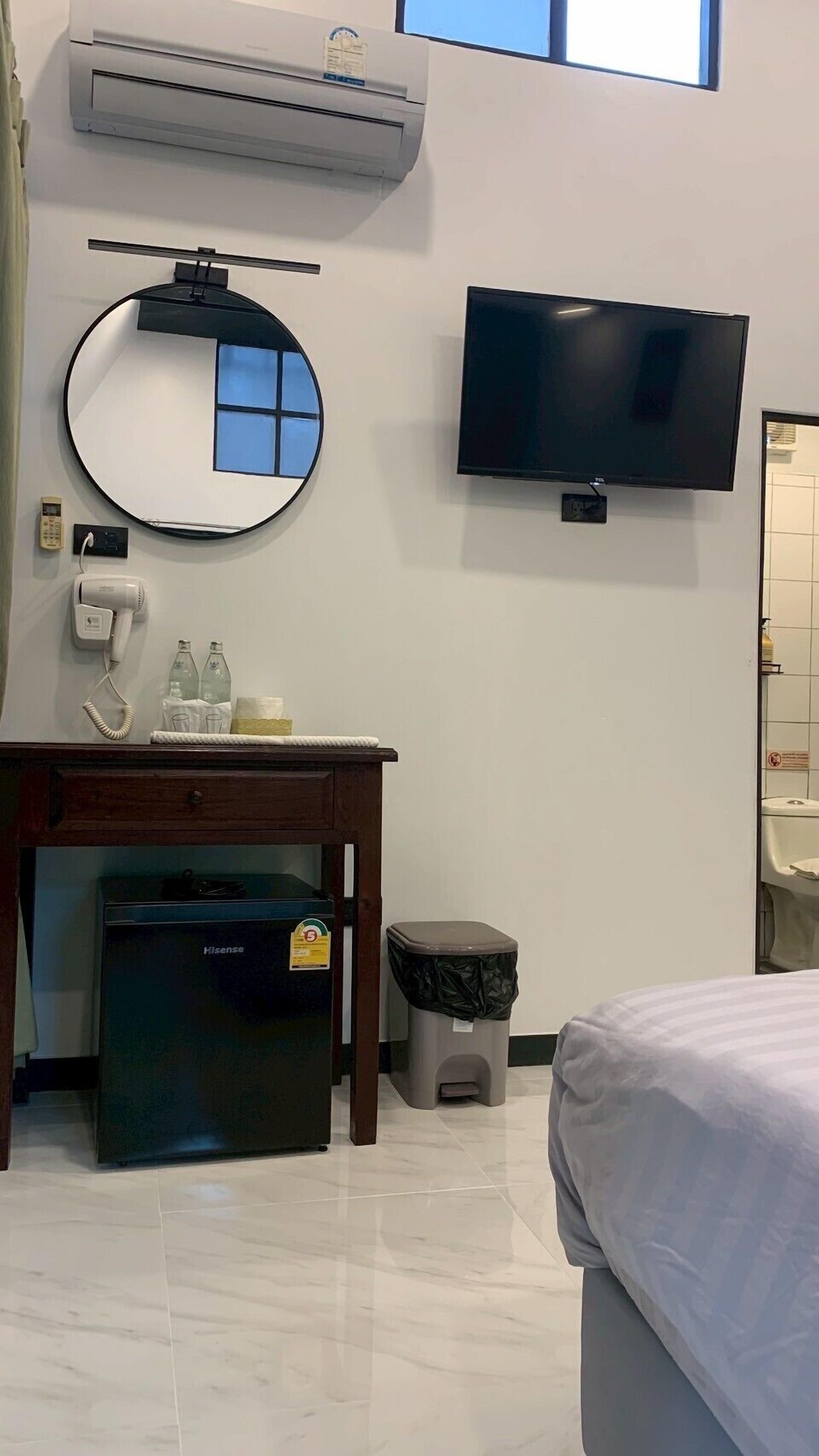 Habitación de hotel con una cama, un escritorio con secador de pelo, un cesto de basura, un refrigerador pequeño, un televisor y un equipo de aire acondicionado.