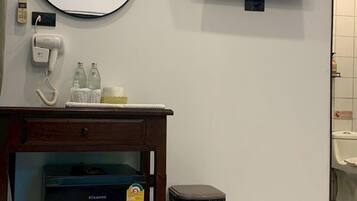 Habitación de hotel con una cama, un escritorio con secador de pelo, un cesto de basura, un refrigerador pequeño, un televisor y un equipo de aire acondicionado.