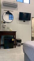 Habitación de hotel con una cama, un escritorio con secador de pelo, un cesto de basura, un refrigerador pequeño, un televisor y un equipo de aire acondicionado.