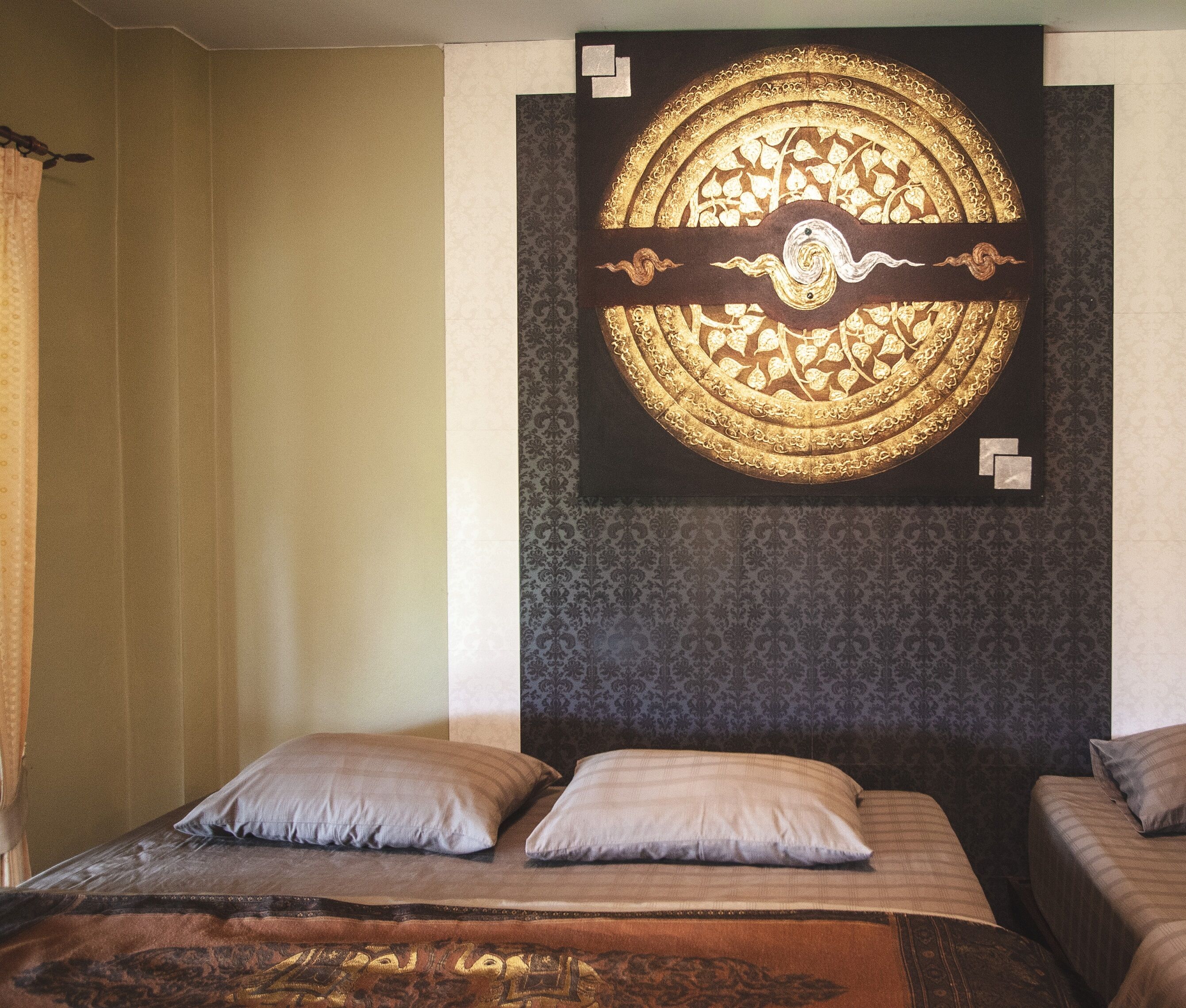 A bedroom with a bed, two pillows, a tapestry with a circular design, and a patterned wall.