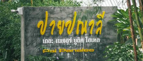 A sign with Thai text, surrounded by greenery.