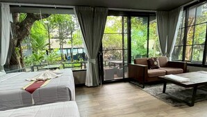 Una habitación amplia con una cama grande, un sofá y una mesita de centro. Cuenta con ventanas grandes con cortinas y vistas a zonas verdes.