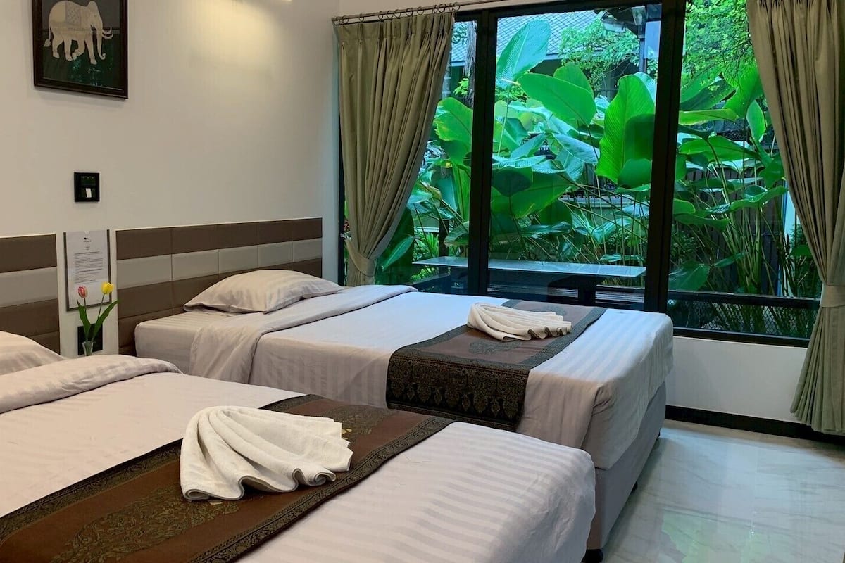 Habitación de hotel con dos camas, una ventana con cortinas, un cuadro en la pared y una planta pequeña.