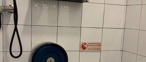 Un baño con un inodoro, un secamanos azul y tres botellas de gel de ducha en un estante.