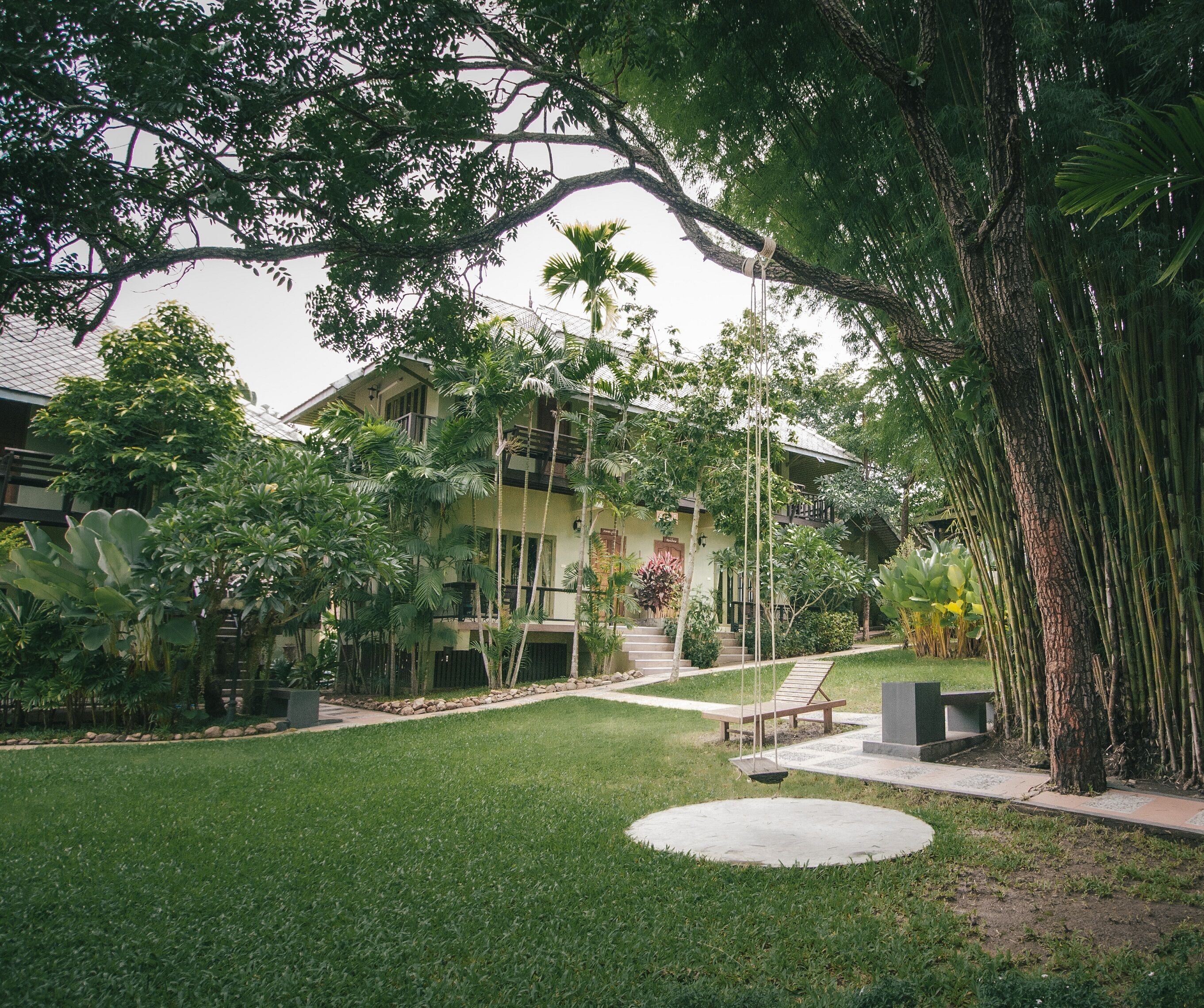 A well-maintained garden with a lawn, a swing chair, and a pathway leading to a building with a balcony.