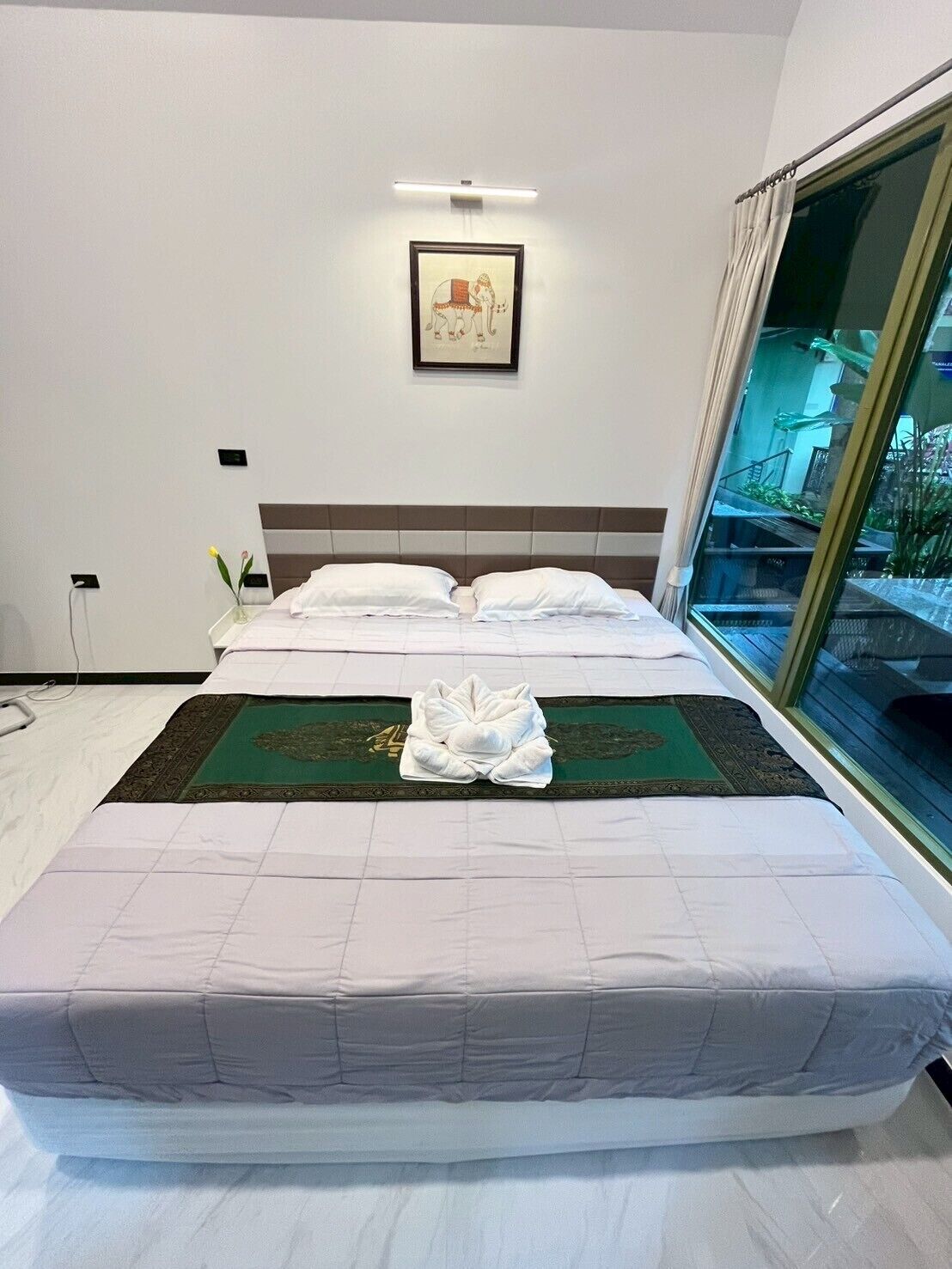A hotel room with a neatly made bed, a framed artwork on the wall, and a view of a building through the window.