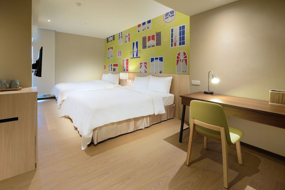 Een hotelkamer met een groot bed, een bureau met stoel, een televisie en een muur met kleurrijke raamdecoraties.