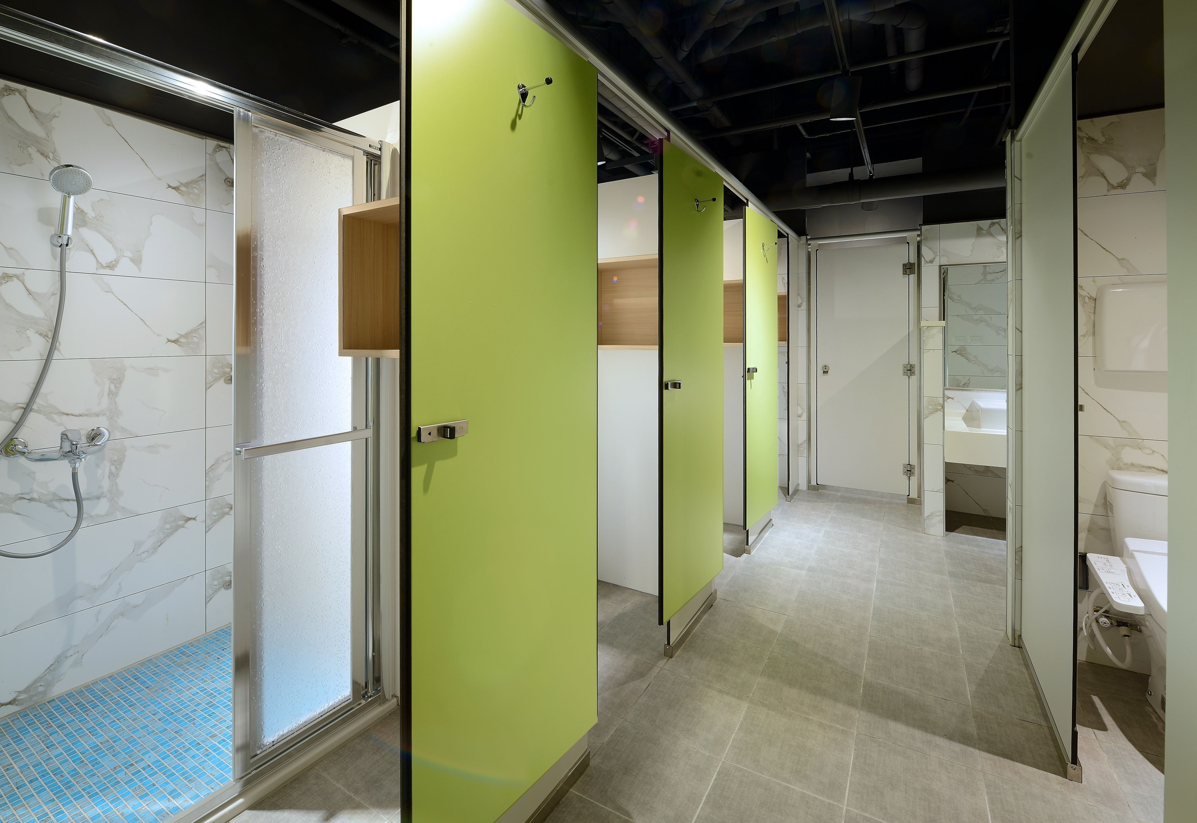 A public restroom with individual stalls, a shower area, and a sink.
