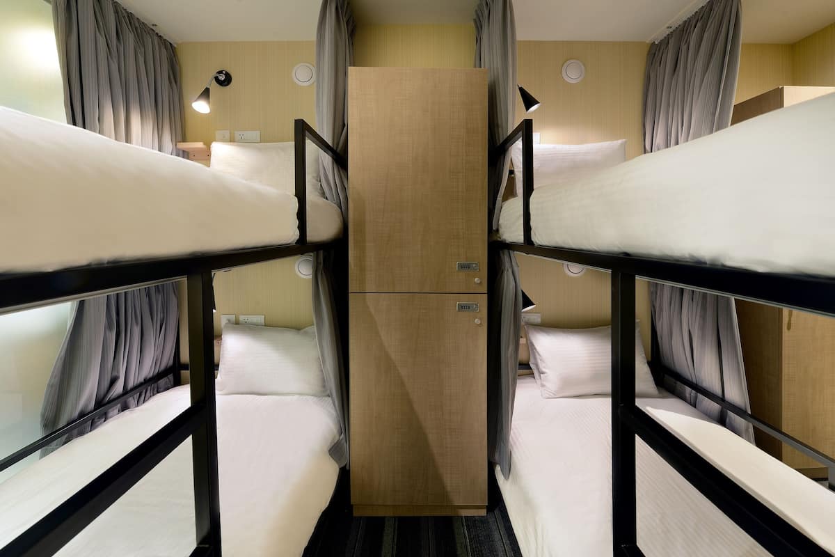 Een slaapkamer met een stapelbed, een houten garderobe, gordijnen en bedlampjes.