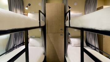 Een slaapkamer met een stapelbed, een houten garderobe, gordijnen en bedlampjes.