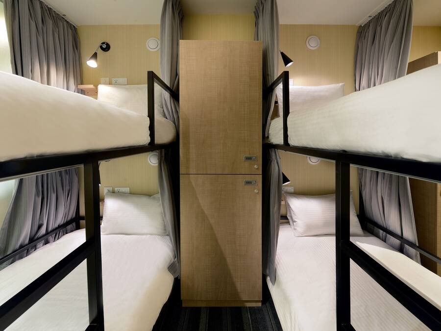 Een slaapkamer met een stapelbed, een houten garderobe, gordijnen en bedlampjes.