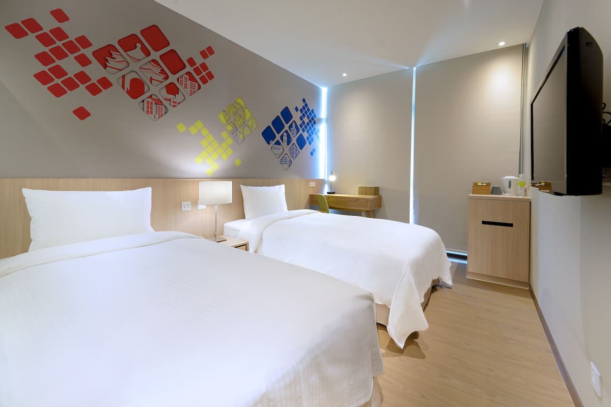 Een hotelkamer met twee bedden, een flatscreen televisie, een bureau met lamp en een muur met geometrische patronen.