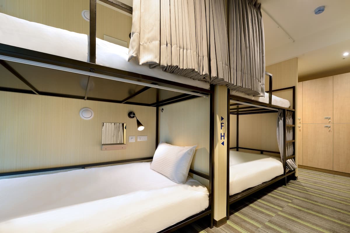 Een slaapkamer met een stapelbed, een hoofdbord, een nachtkastje met lamp en een garderobe.
