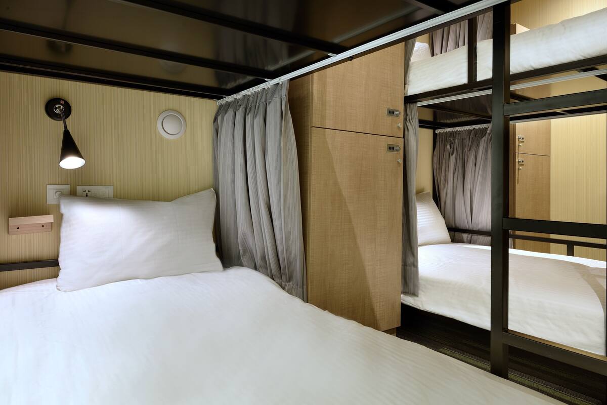 Een slaapkamer met een stapelbed, een houten hoofdbord, een bedlampje en een gordijn.