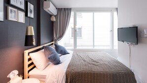 A hotel room with a large window, a bed with a headboard, a flat-screen TV mounted on the wall, and framed pictures on the wall. - Mono House Hongdae 2 (Seoul)