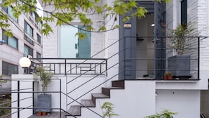 Edifici modern amb una escala que condueix a un balcó, envoltat de vegetació i un cel blau.
