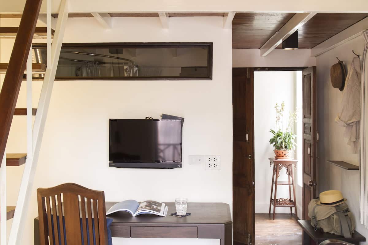 Un dormitorio estilo loft con una cama litera, un escritorio con silla, un televisor y una escalera.