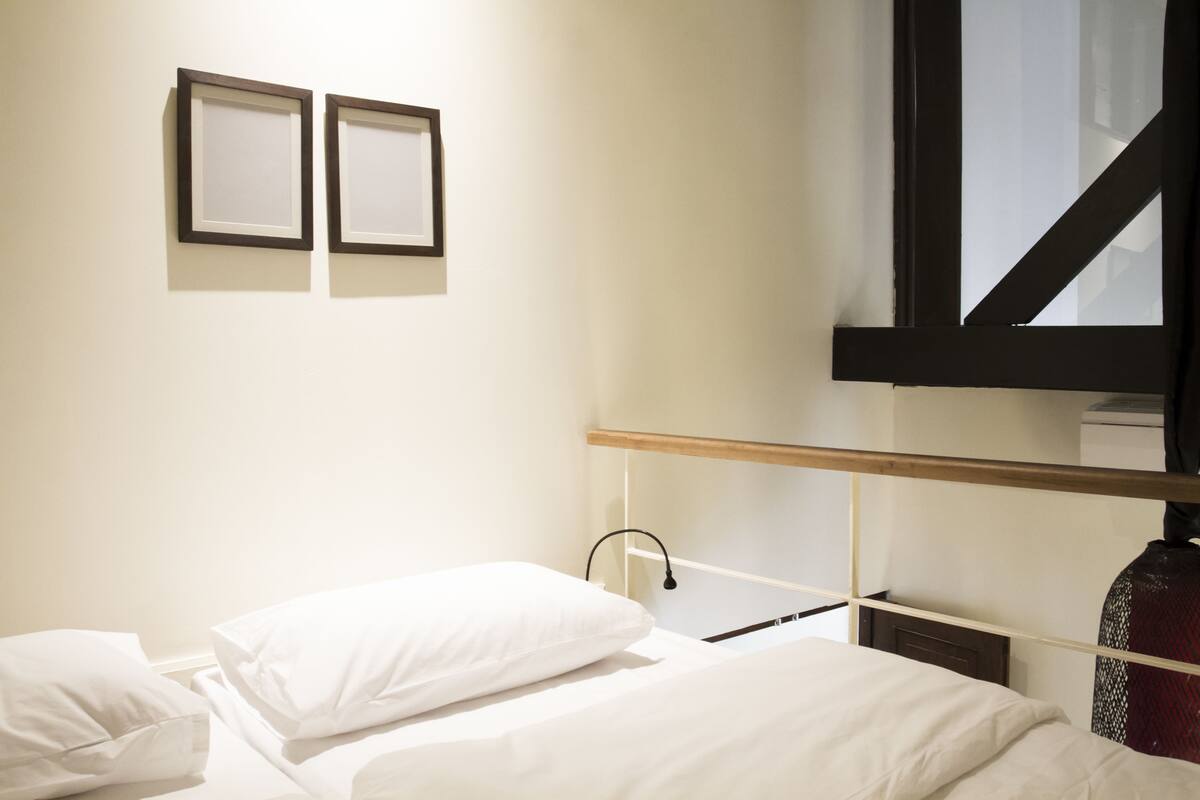 Habitaci ón de hotel con cama, almohadas blancas, cabecero de madera, televisor montado en la pared y dos cuadros enmarcados.