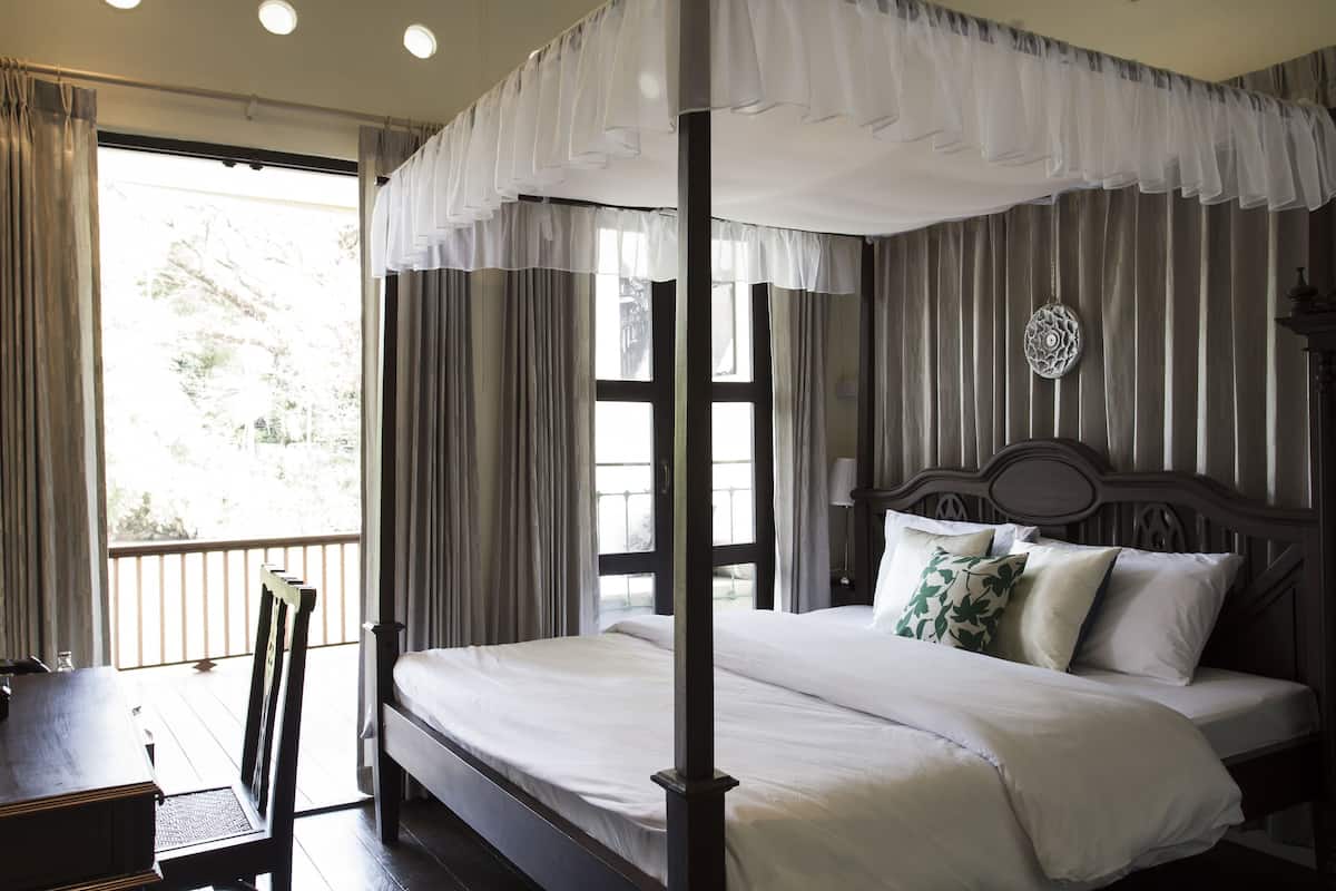 Una cama con dosel, ropa de cama blanca, un cabecero de madera y vistas al exterior a través de amplios ventanales.