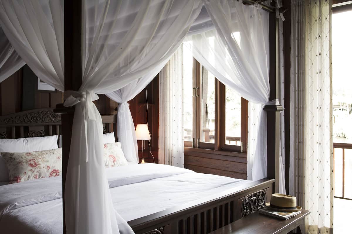 Una cama con dosel, una mesita de noche con lámpara y una ventana con cortinas.