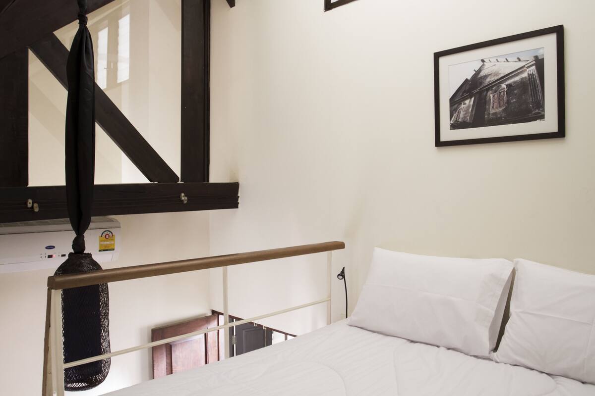Un dormitorio con cama, un cuadro enmarcado en la pared y una ventana con vista a un edificio.