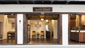 The entrance of a historic Thai hotel with a traditional wooden facade, a reception desk, and a seating area with chairs and a small table. - Baan Luang Rajamaitri Historic Inn (Chanthaburi)