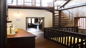 A spacious interior with a wooden staircase, a reception desk, and a view of the reception area. - Baan Luang Rajamaitri Historic Inn (Chanthaburi)