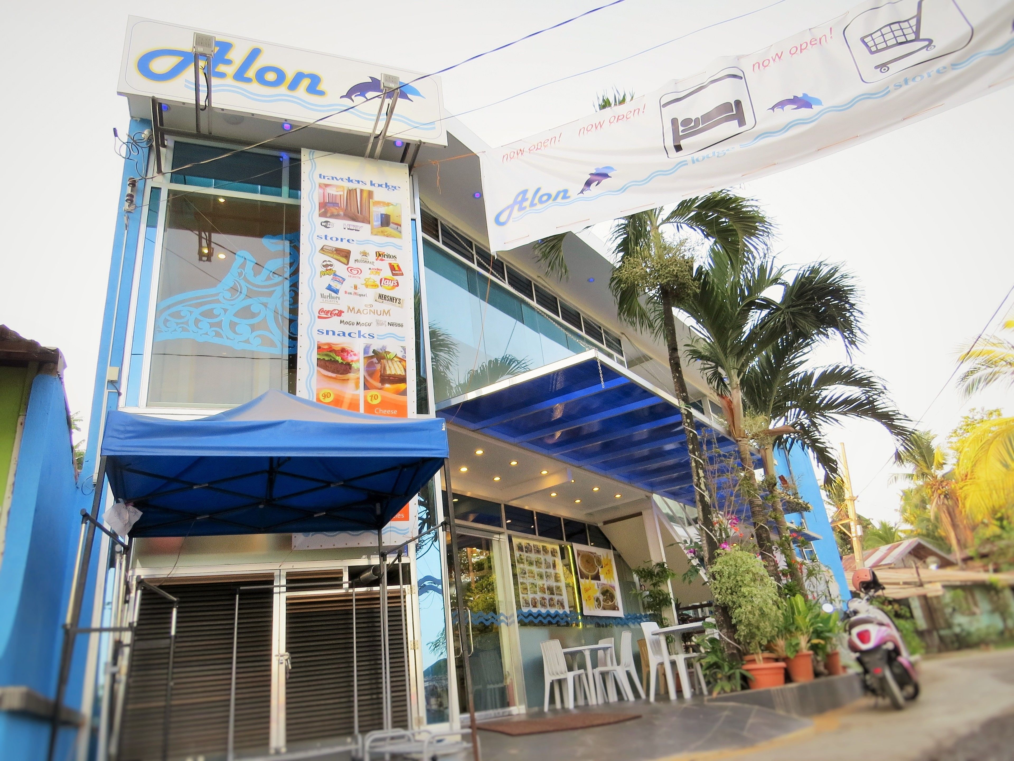 A two-story building with a sign reading "Alon" and a banner advertising a store and snacks.