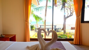 A hotel room with a bed, a window with curtains, and a view of the beach and palm trees. - New Travel Beach Resort (Tha Mai)