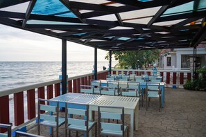 Eine Terrasse am Meer mit Tischen und Stühlen, einem Geländer und Blick auf den Ozean.