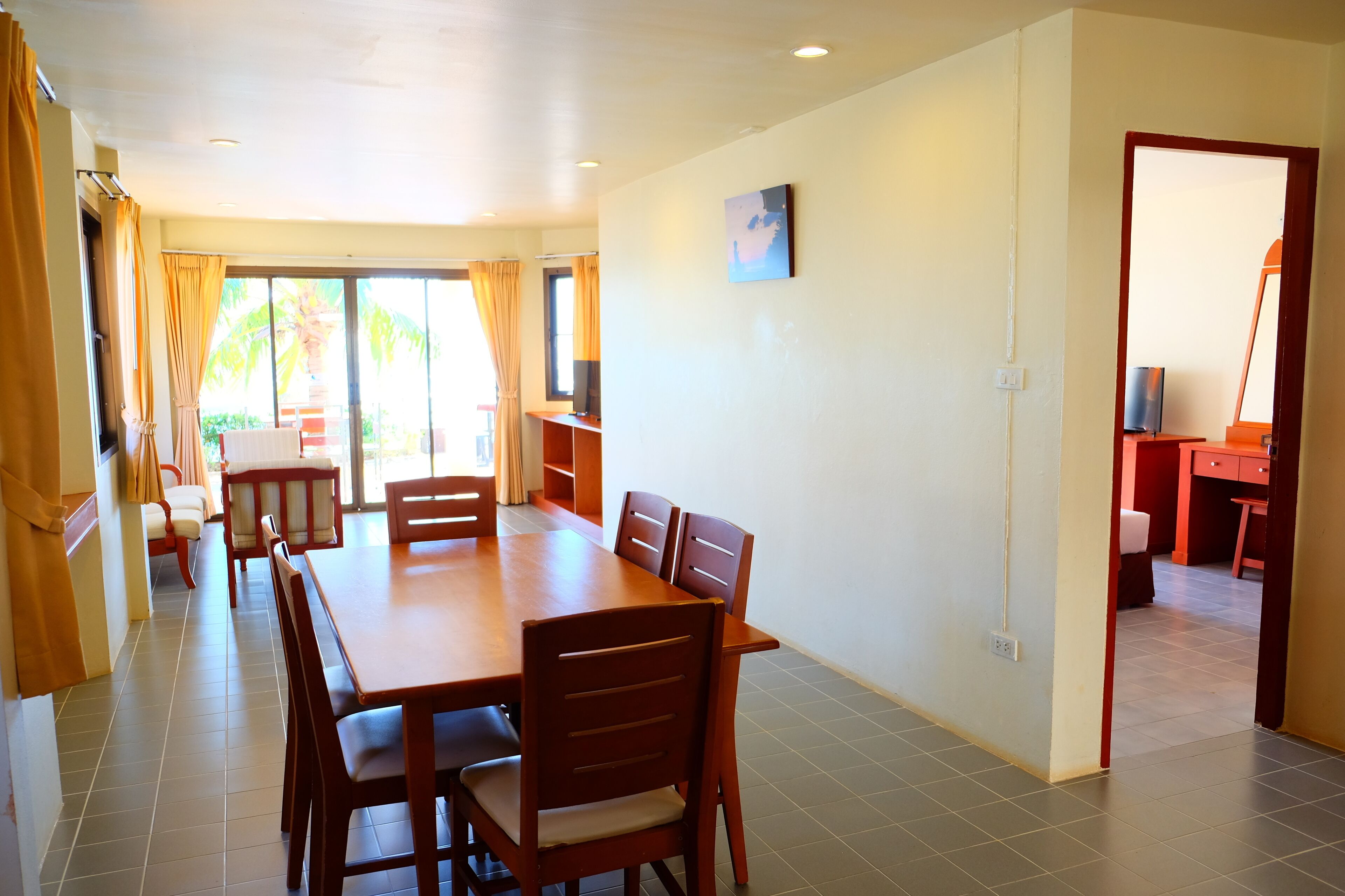 A dining area with a large wooden table and chairs, a TV on a stand, and a view through a glass door to an outdoor area.