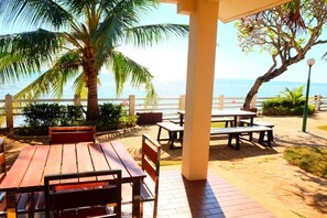 Eine Terrasse im Freien mit Holztischen und -bänken, einer Palme und Blick aufs Meer.