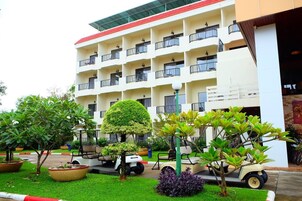 Un hotel de varios pisos con techo plano, balcones y un jardín bien cuidado con diversas plantas y un carrito de golf.