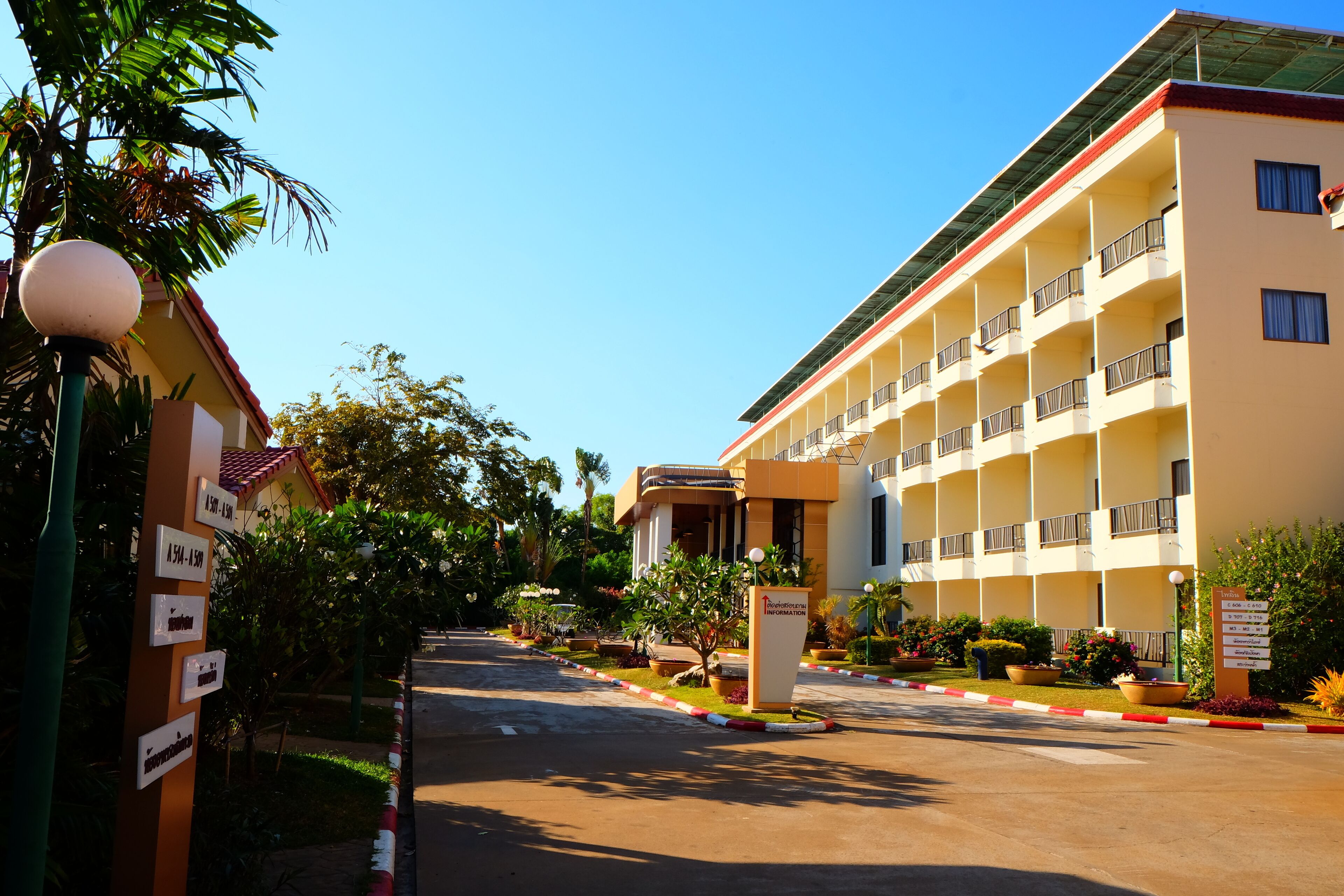 A multi-story hotel with a central entrance, surrounded by lush greenery and a clear sky.