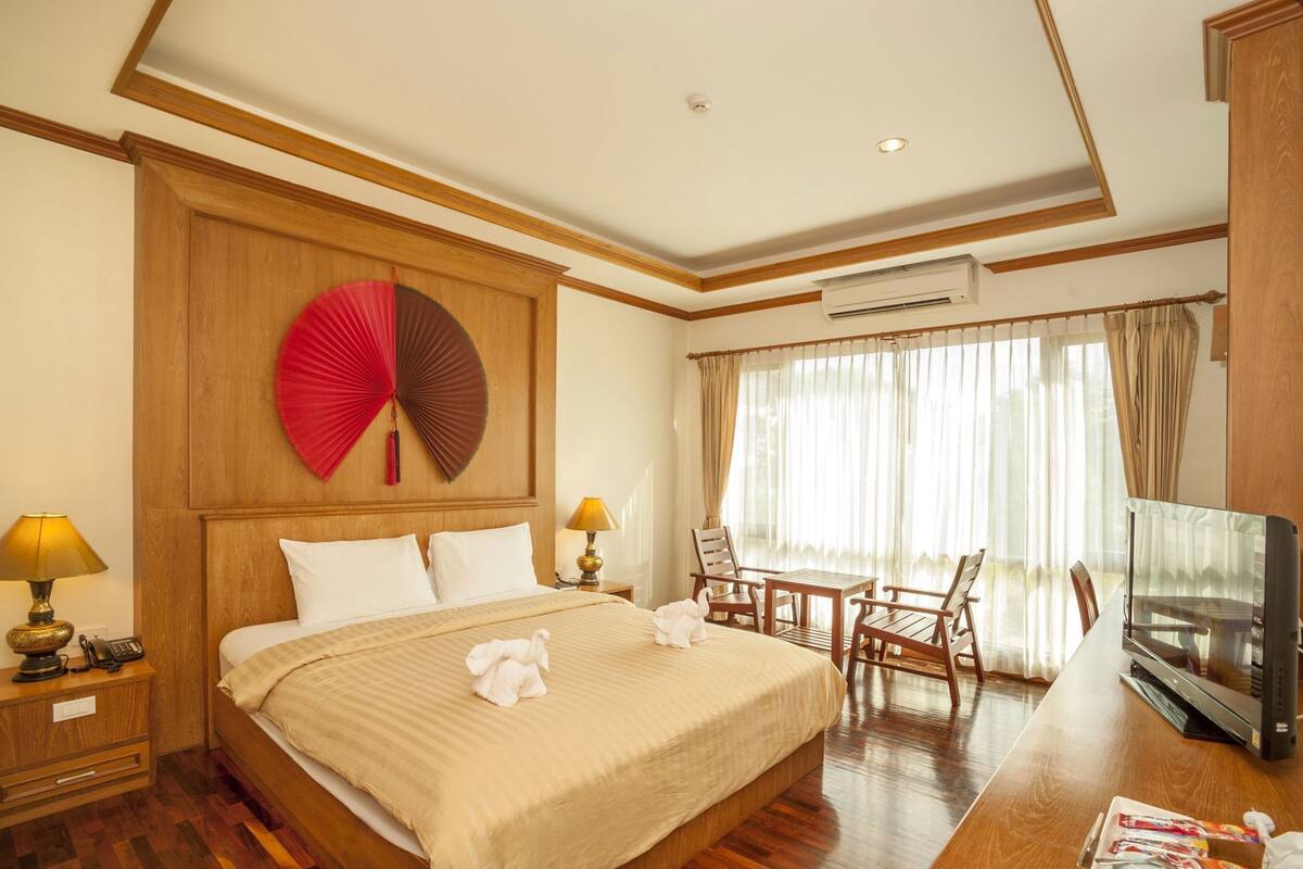 A hotel room with a bed, bedside lamps, a TV, a desk with chairs, and a large window with curtains.