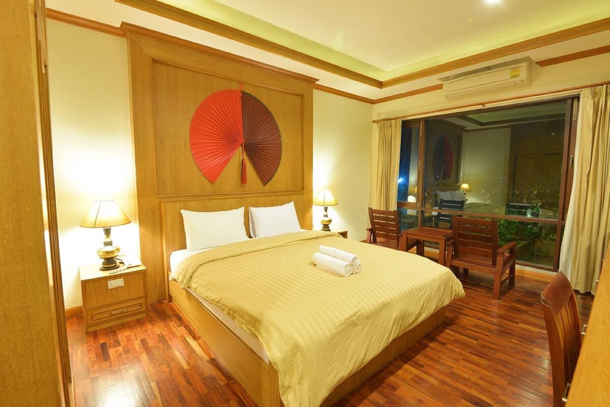 A hotel room with a large bed, wooden headboard, two bedside tables with lamps, a wooden chair, and a balcony with a view.