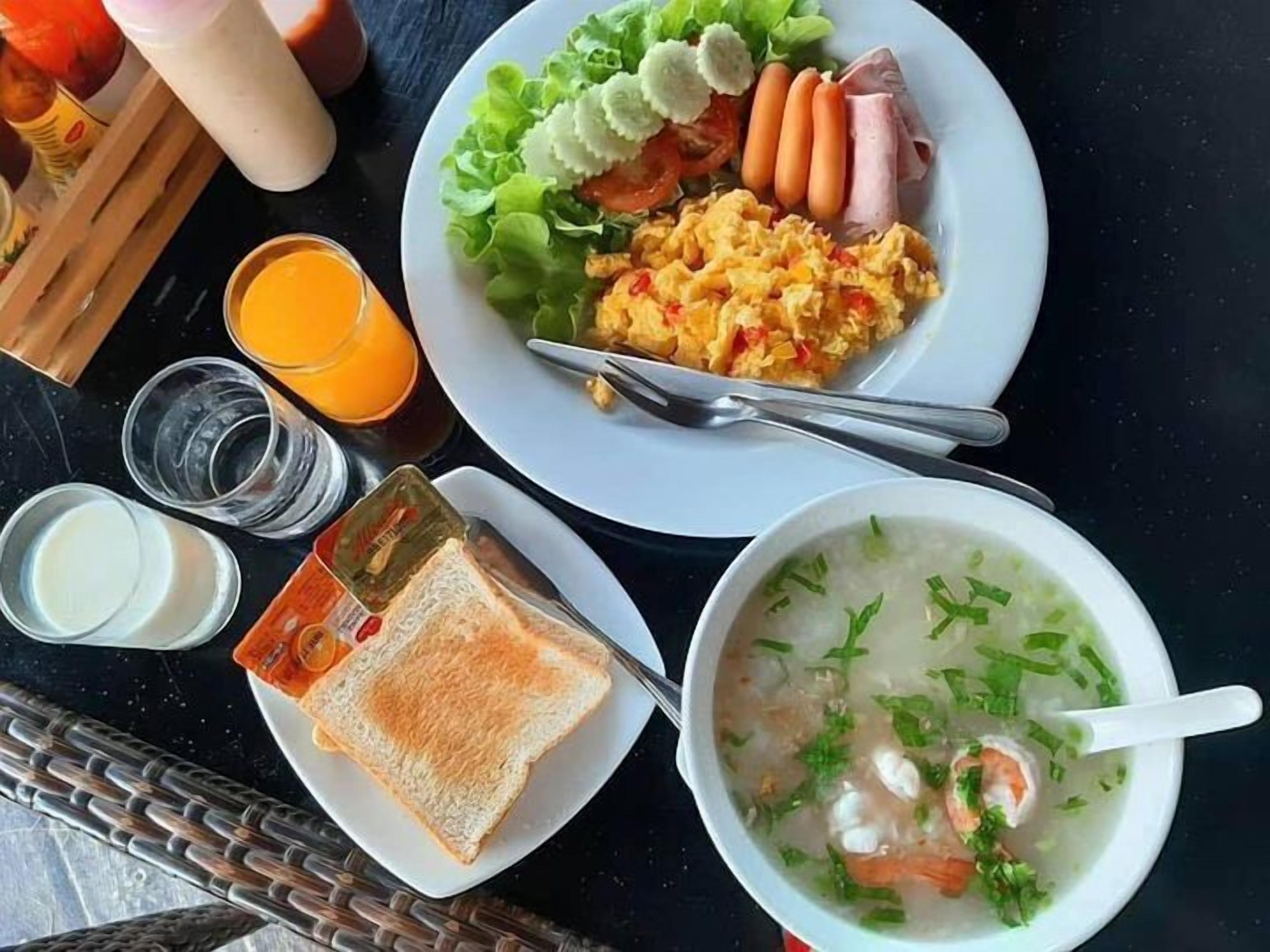 Un plato de desayuno con huevos revueltos, salchichas y jamón, un tazón de sopa de camarones y un vaso de jugo de naranja.