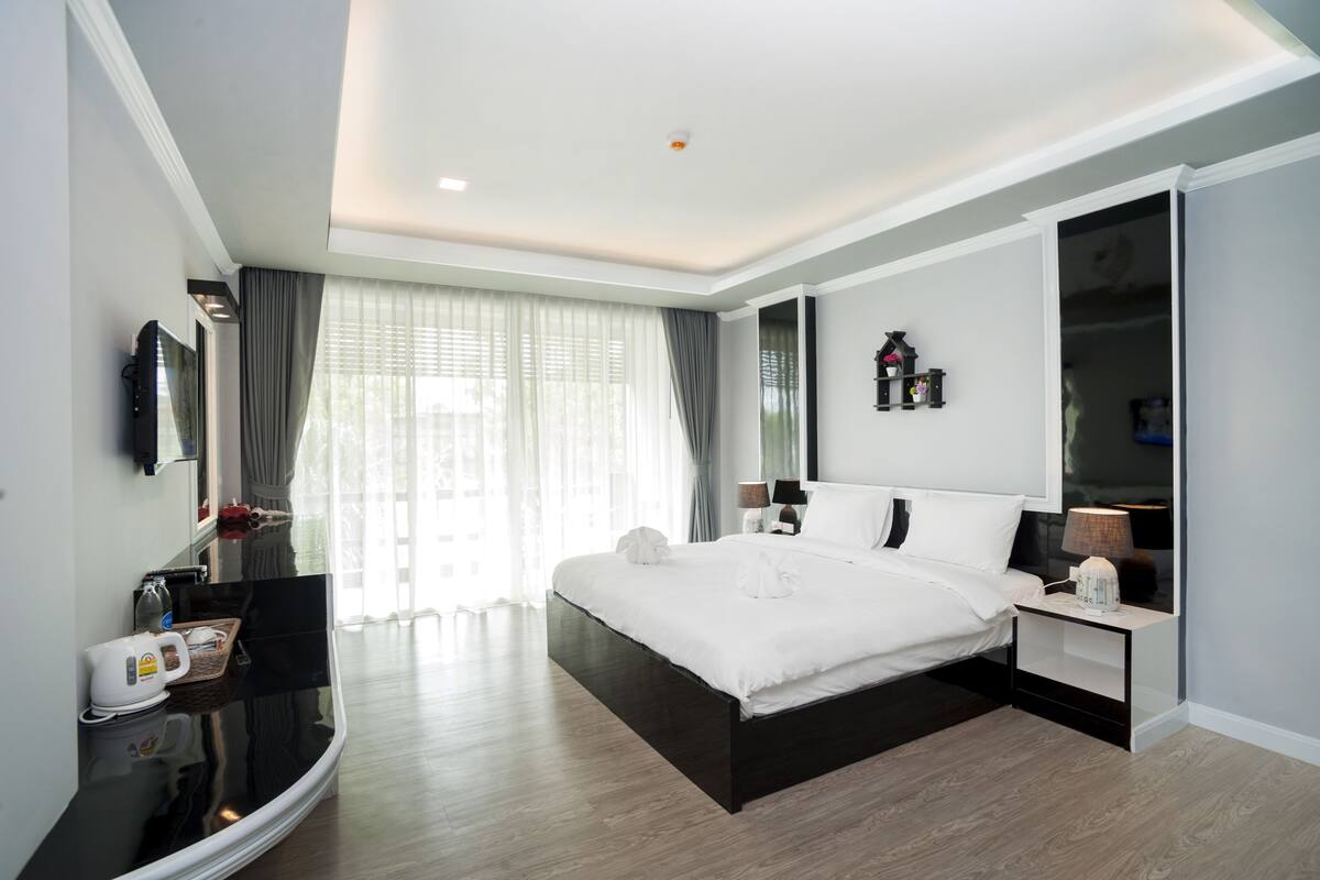 A modern hotel room with a large bed, bedside tables, a flat-screen TV, and a wardrobe.