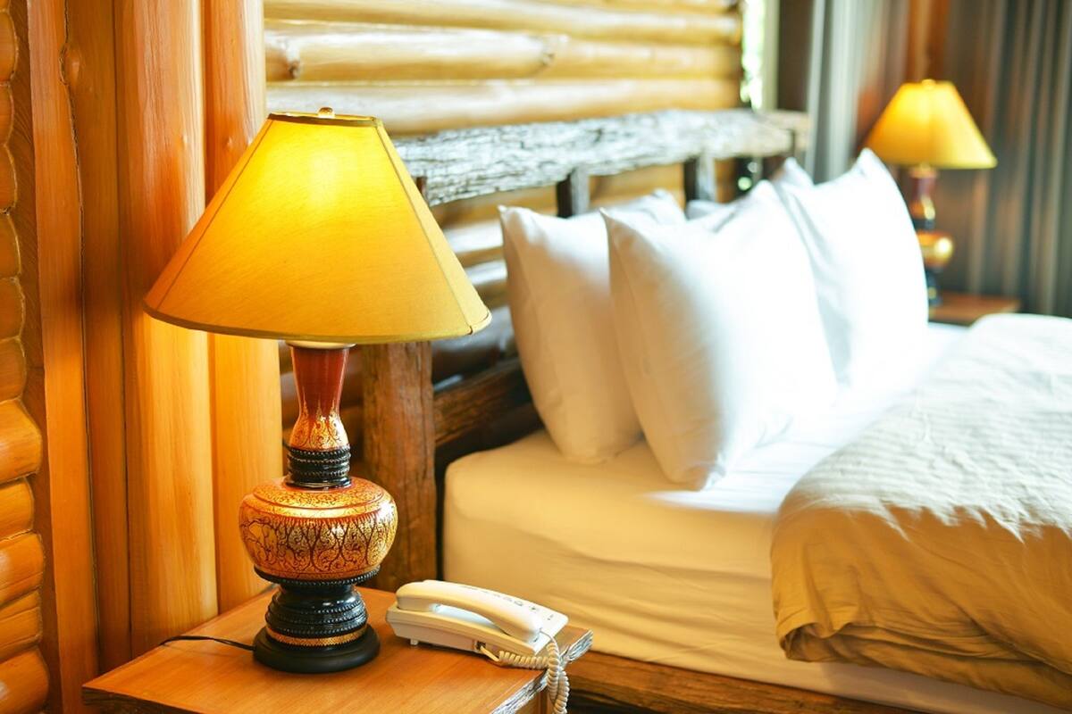 A hotel room with a wooden headboard, a bedside lamp, a telephone, and a bed with white bedding.