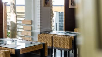 A restaurant with wicker chairs, glass tables, and a view of the outdoors.