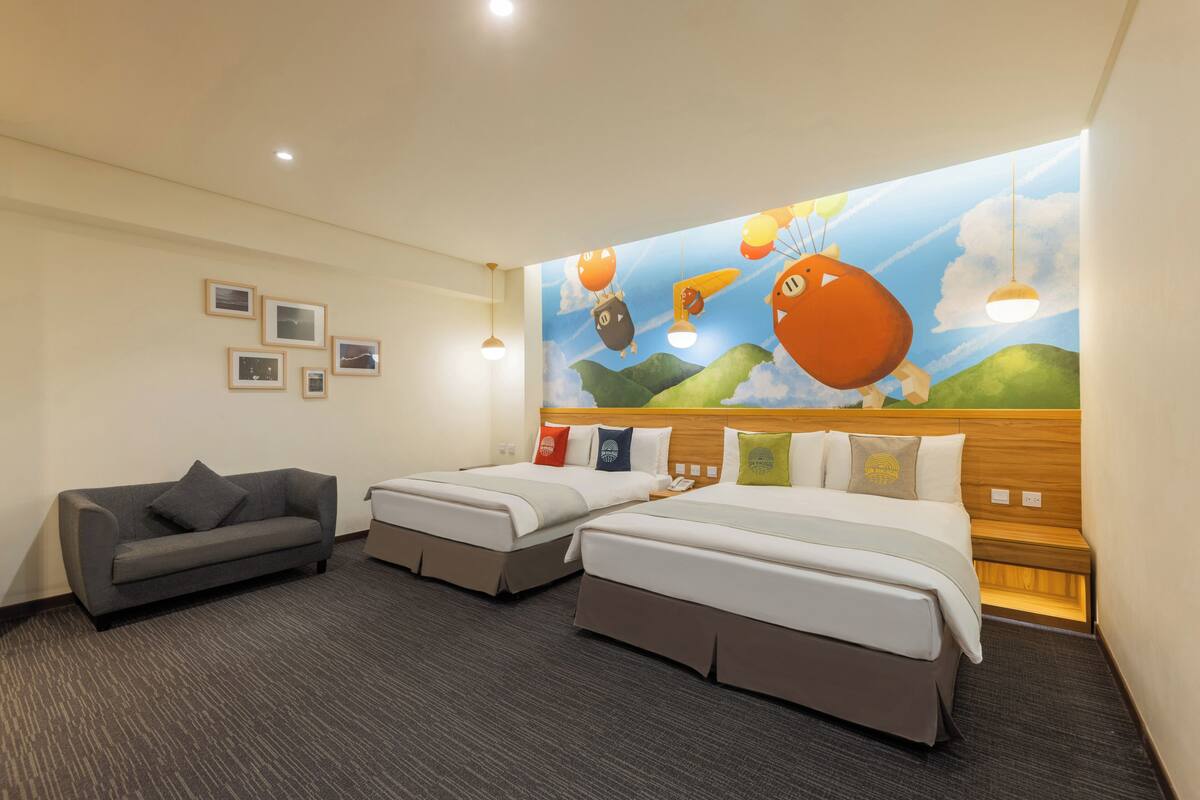 A hotel room with two beds, a sofa, and a mural of balloons and clouds on the wall.